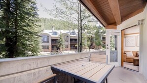 A wooden deck with a table and benches, overlooking a building with multiple balconies and a forested area.