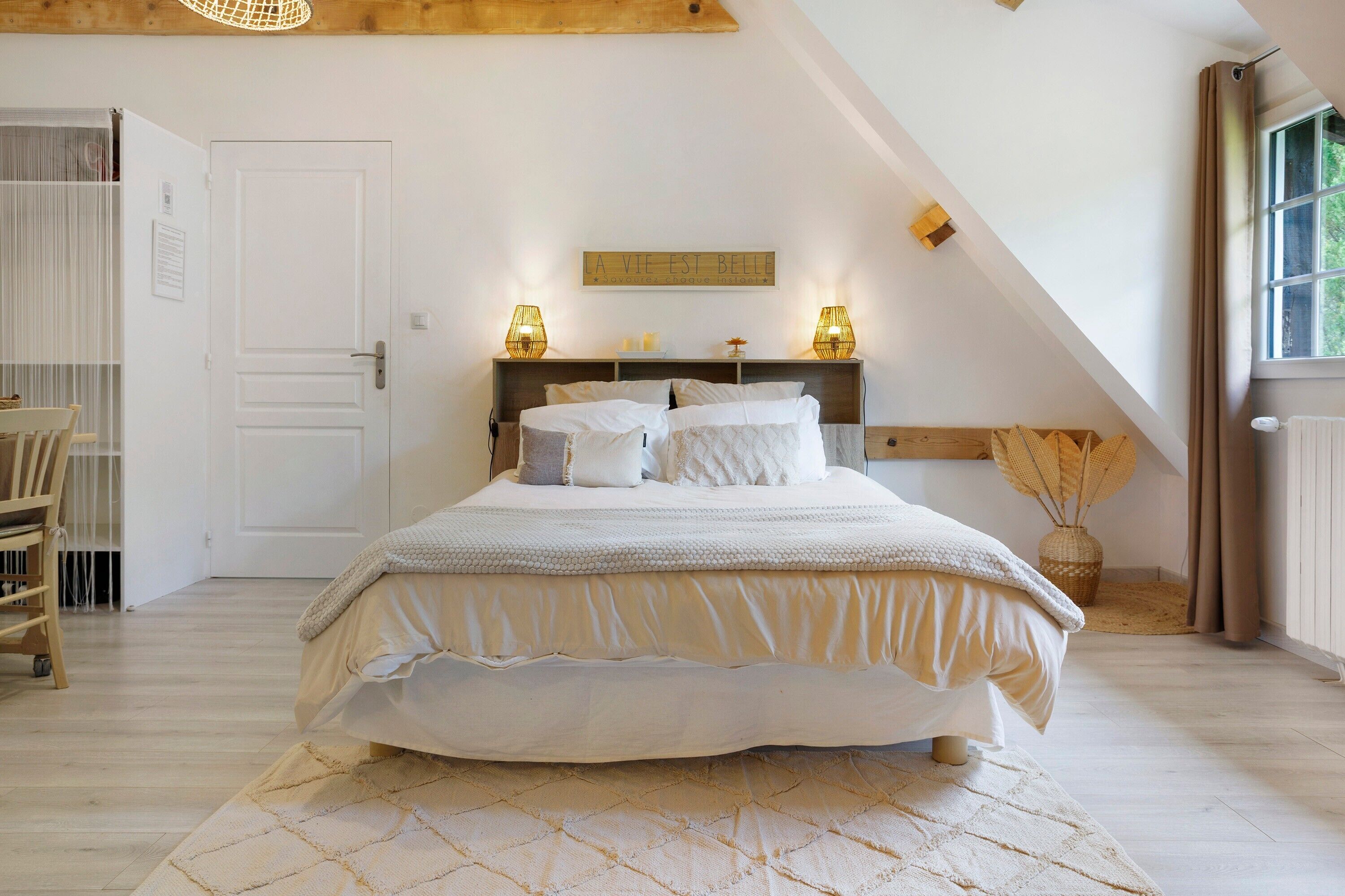 Une chambre à coucher avec un lit, une table de chevet, une lampe, une fenêtre et une porte.
