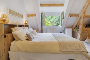 A bedroom with a bed, bedside lamps, a window, and a view of greenery.
