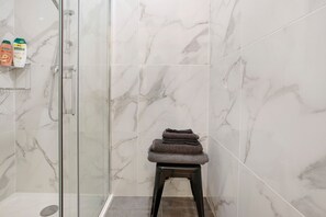 A bathroom with marble walls, a glass shower enclosure, and a small stool with folded towels. - Maraval – Cozy air-conditioned suite in a private home with garden and pool access in Périgueux (Trélissac)