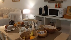 Disposição para o café da manhã, com mesa, alimentos, micro-ondas e uma sala de estar acolhedora com sofá e luminária.