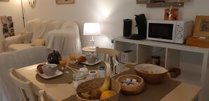 A breakfast setup with a table, breakfast items, a microwave, and a cozy living area with a couch and lamp. - Maraval – Cozy air-conditioned suite in a private home with garden and pool access in Périgueux (Trélissac)