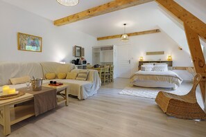 A cozy loft-style bedroom with a bed, a sofa, a dining table, and a wicker chair. - Maraval – Cozy air-conditioned suite in a private home with garden and pool access in Périgueux (Trélissac)