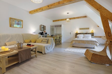 A cozy loft-style bedroom with a bed, a sofa, a dining table, and a wicker chair.. Maraval – Cozy air-conditioned suite in a private home with garden and pool access in Périgueux