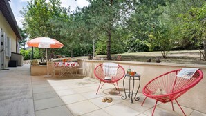 Um pátio externo com mesa, cadeiras e um guarda-sol vermelho.