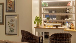 A well-lit bar area with shelves of bottles and glasses, a potted plant, and wicker chairs. - Elivaas Opalys (Arpora)