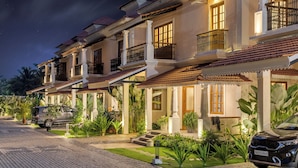 A row of traditional-style villas with balconies, a paved driveway, and lush greenery. - Elivaas Opalys (Arpora)