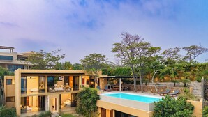 A modern two-story house with a swimming pool, outdoor seating, and lush greenery.