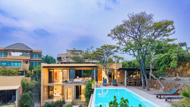 A modern two-story house with a swimming pool, outdoor seating, and lush greenery.