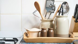 A kitchen counter with a wooden tray holding kitchen utensils, a white ceramic jar, and two brown spice jars.