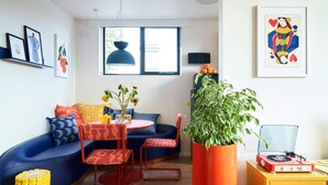 A modern living room with a blue sofa, a round table with chairs, a potted plant, and a mustard-colored cabinet.
