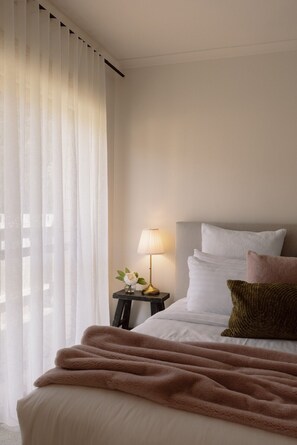 A neatly made bed with a fluffy blanket, a bedside lamp, and a vase with flowers on a small table beside it. - Nancy’s of Trentham | Stylish 3BD Walk to Town (Trentham)