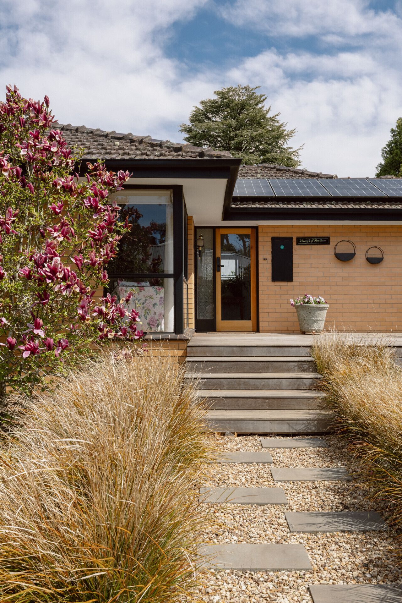 A modern house with a brick exterior, a glass door entrance, and a solar panel roof.