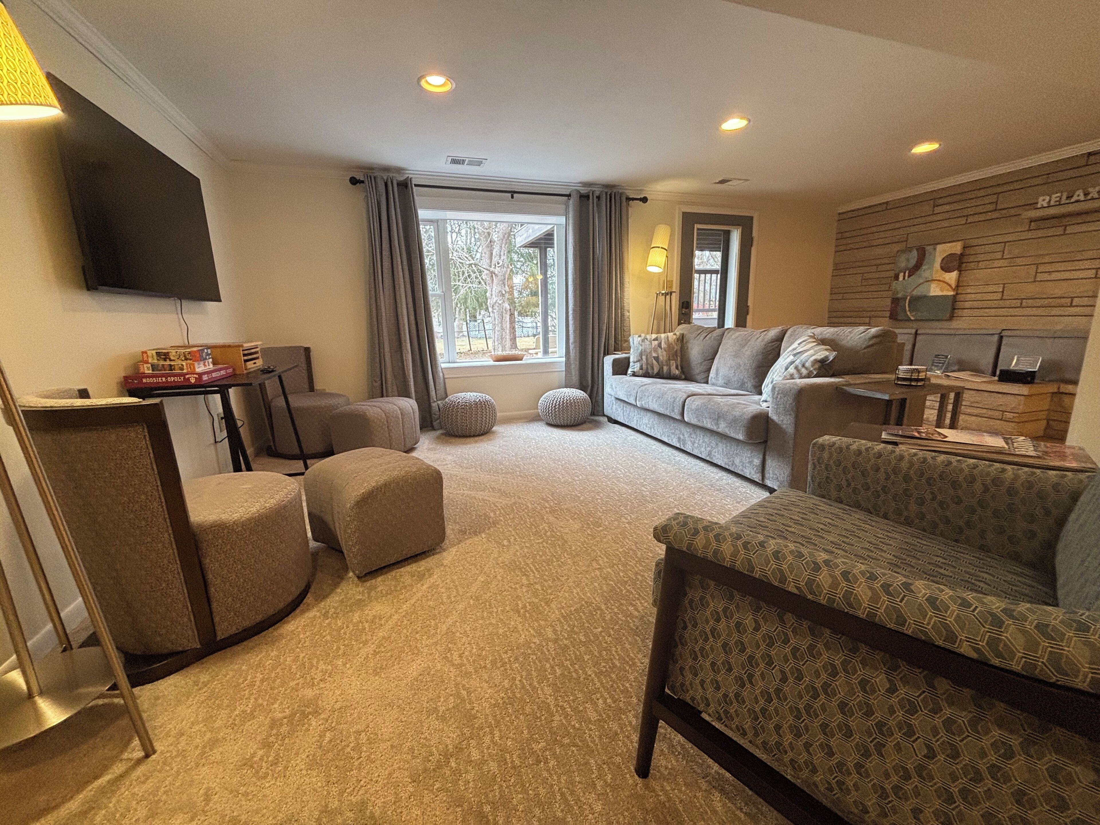 A cozy living room with a sofa, ottomans, a coffee table, and a flat-screen TV mounted on the wall.