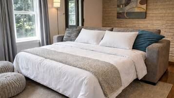 A bedroom with a large bed, a grey sofa, a woven throw blanket, and a stone wall with a painting.