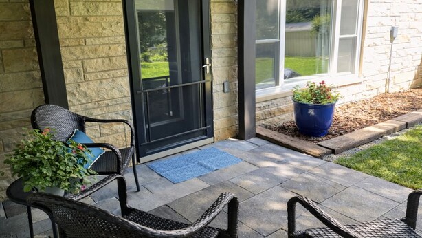 A patio with two wicker chairs, a black door, and a blue potted plant. - Stadium Stroll | Walk to IU Football | Sleeps 14 (Bloomington)