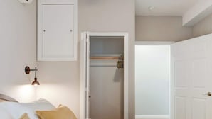 Quarto com cama, almofadas, luminária na parede, guarda-roupa e porta que dá para outro cômodo.