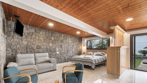A modern bedroom with a stone wall, a bed, a sofa, and a TV. - 'Vista Teide' Vacation Apartment with Sea View, Wi-Fi, and Air Conditioning (Tacoronte)