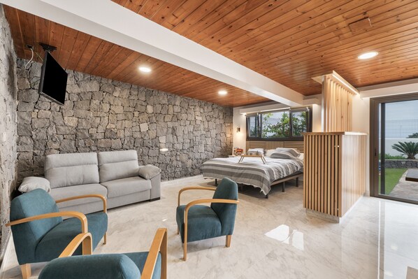 Une chambre moderne avec un mur en pierre, un lit, un canapé et un téléviseur.