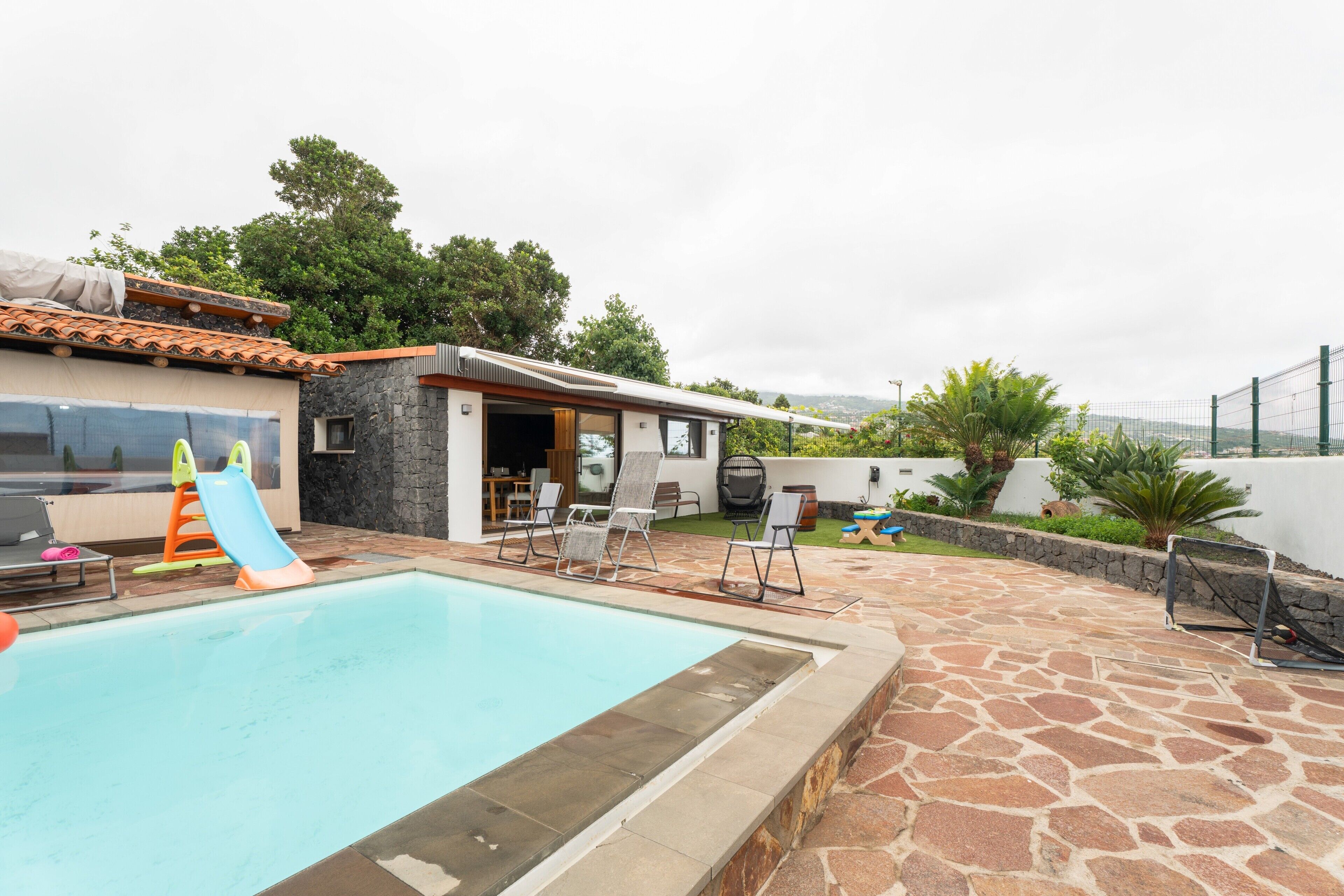 A swimming pool with lounge chairs, a slide, and a stone patio.