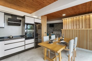 Une cuisine moderne avec un plafond en bois, un coin repas avec une table et des chaises en bois, et un mur en pierre en arrière-plan.