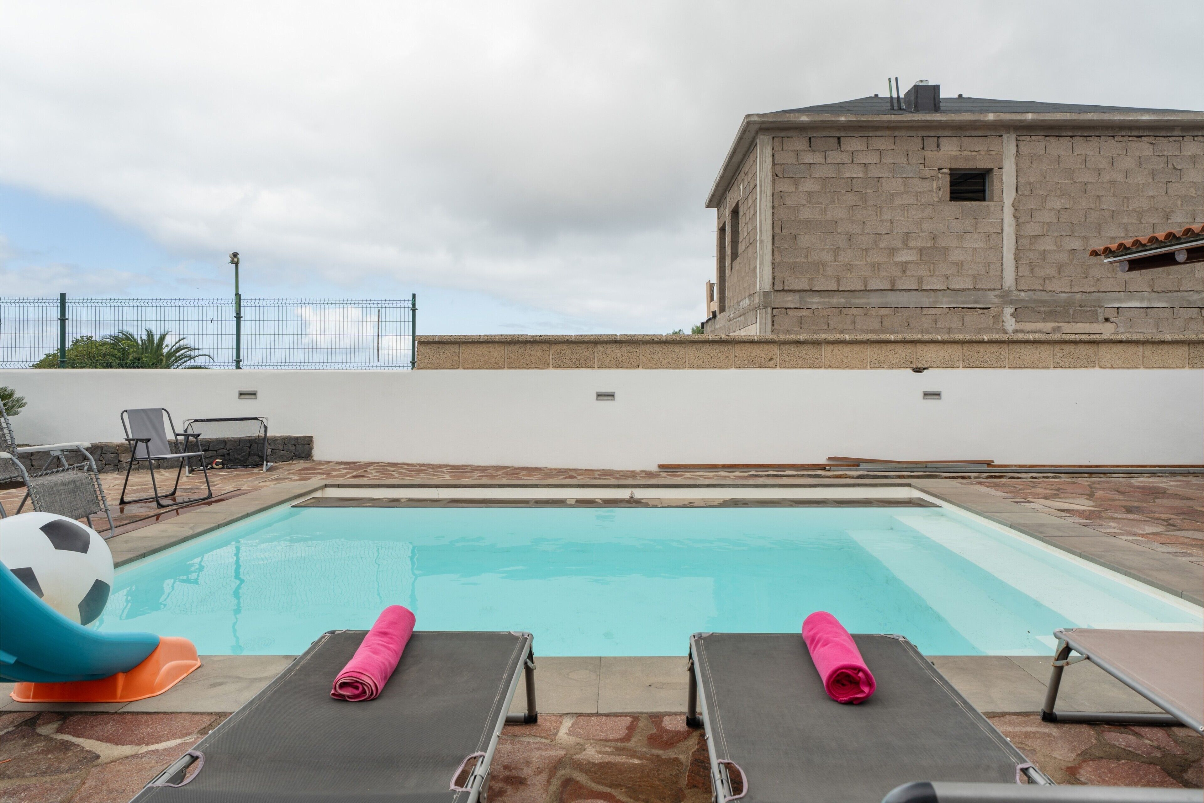 A swimming pool with lounge chairs and a soccer ball.