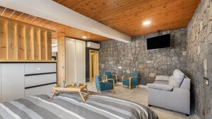 A bedroom with a bed, a stone wall, a flat-screen TV, and a gray sofa. - 'Vista Teide' Vacation Apartment with Sea View, Wi-Fi, and Air Conditioning (Tacoronte)