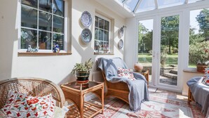 Una habitación soleada con muebles de mimbre, una mesa de cristal y una alfombra estampada.