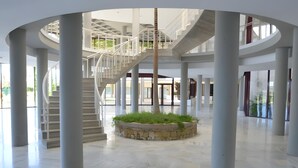 Un amplio atrio con una escalera central, grandes columnas y una jardinera circular con plantas.