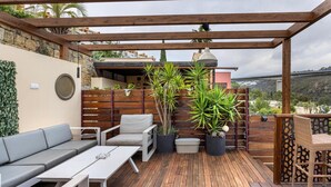 Un patio techado al aire libre con suelo de madera, arreglos de asientos y plantas en macetas.