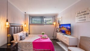 Un dormitorio moderno con cama, mesita de noche, televisión y ventana con persianas.