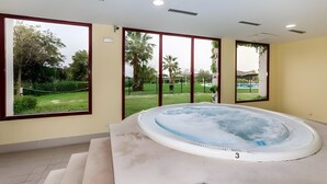 Un cuarto de spa con hidromasaje, ventanas amplias y vistas a un jardín ajardinado.