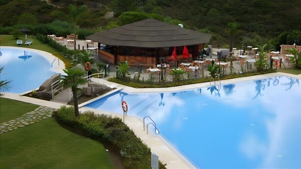 Un resort con una gran piscina, mobiliario exterior y un edificio de techo oscuro.