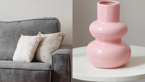 Un sofá gris con dos almohadas y un florero rosa sobre una mesa blanca.