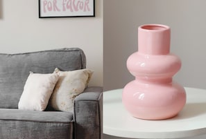 Ein graues Sofa mit zwei Kissen und einer rosa Vase auf einem weißen Tisch.
