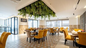 A modern dining area with yellow chairs and tables, large windows, and hanging plants. - visit hotel (Riyadh)