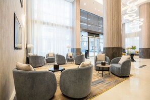 A spacious lobby with grey upholstered chairs, a central coffee table, and a large window with sheer curtains. - Visit Hotel (Riyadh)