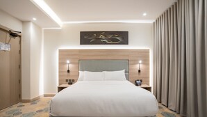 A modern hotel room with a large bed, wooden headboard, two bedside tables with lamps, and a large window with curtains. - visit hotel (Riyadh)