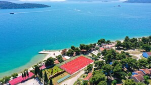 Vue aérienne d’une zone côtière avec une plage, un court de tennis et des bâtiments environnants.