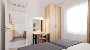 A hotel room with a bed, a desk with a chair, a wardrobe, and a window.