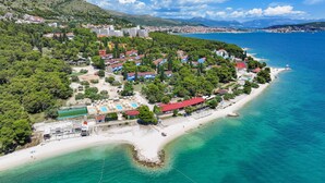 An aerial view of a coastal resort with multiple buildings, a beach, and clear blue waters.