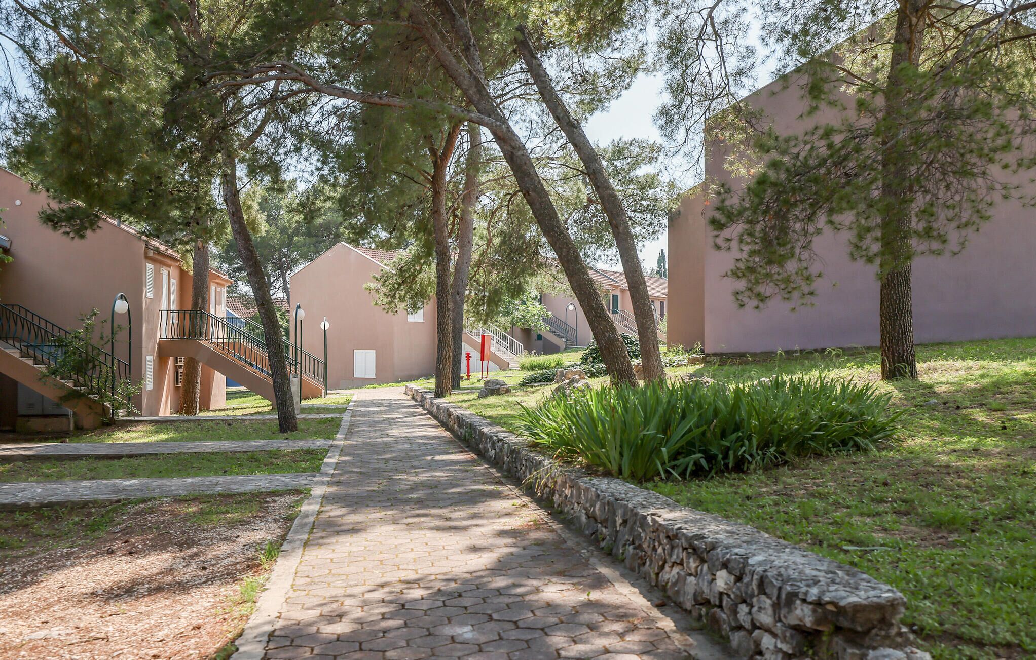 A paved pathway leading to a building with a stone wall on one side and a staircase on the other.