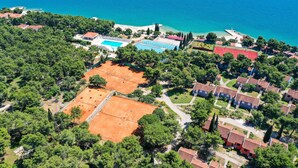 Vue aérienne d’un quartier résidentiel situé sur la côte, avec des maisons, un court de tennis et une piscine.