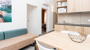 Une cuisine moderne équipée d’un four à micro-ondes, d’une machine à café et d’une bouilloire sur le plan de travail. On y trouve une table à manger en bois, un panier en fil métallique et un banc avec un coussin. Un tableau représentant un paysage de montagne est accroché au mur.