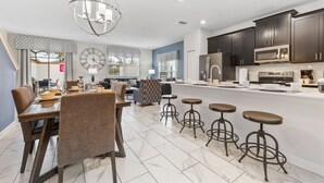 A modern kitchen with dark cabinets, a microwave, and a refrigerator. There is a dining area with a table and chairs, and a bar area with stools. - 8917 Stinger Drive (Davenport)