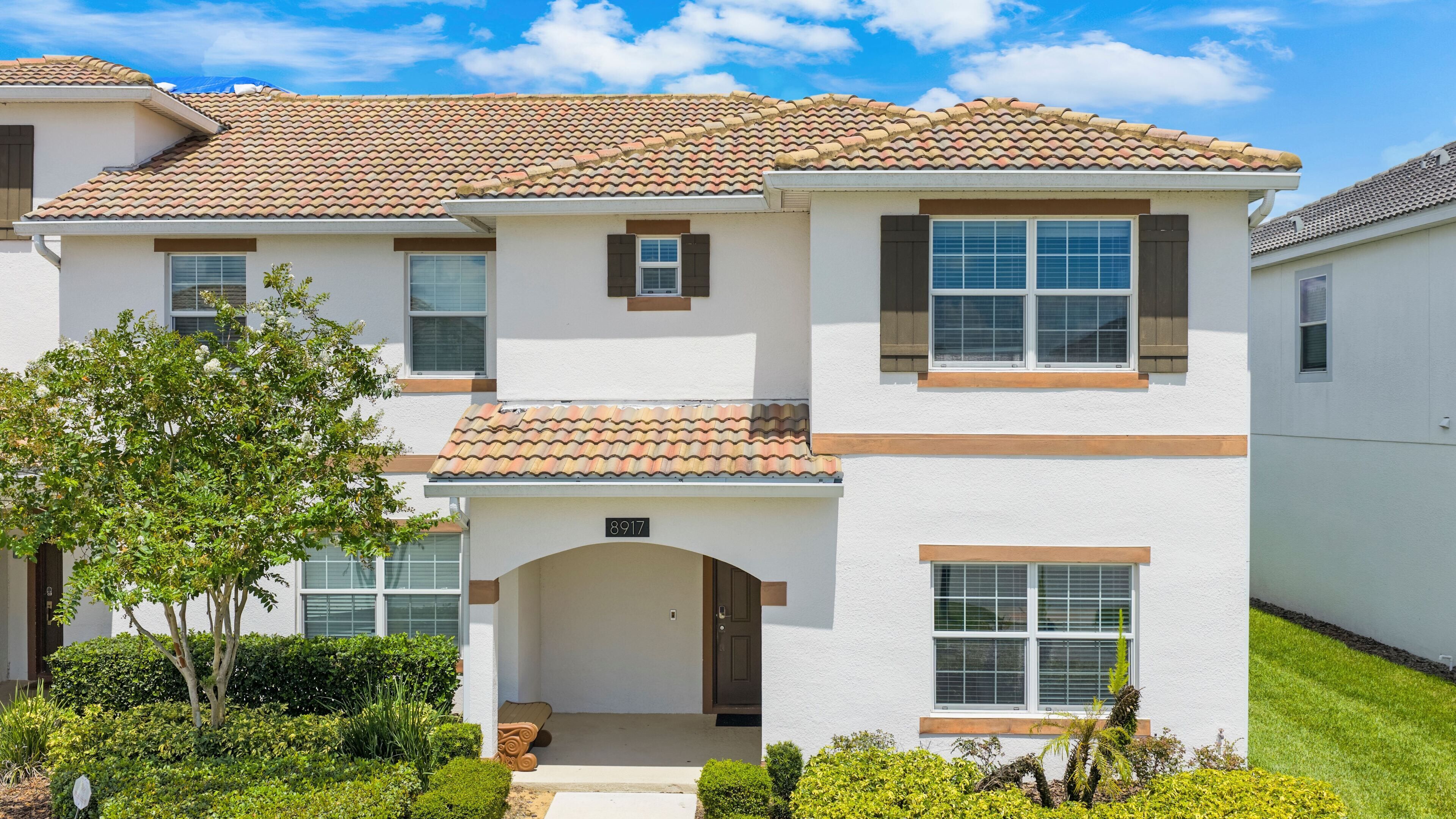A two-story house with a tiled roof, a front porch, and a well-maintained lawn.