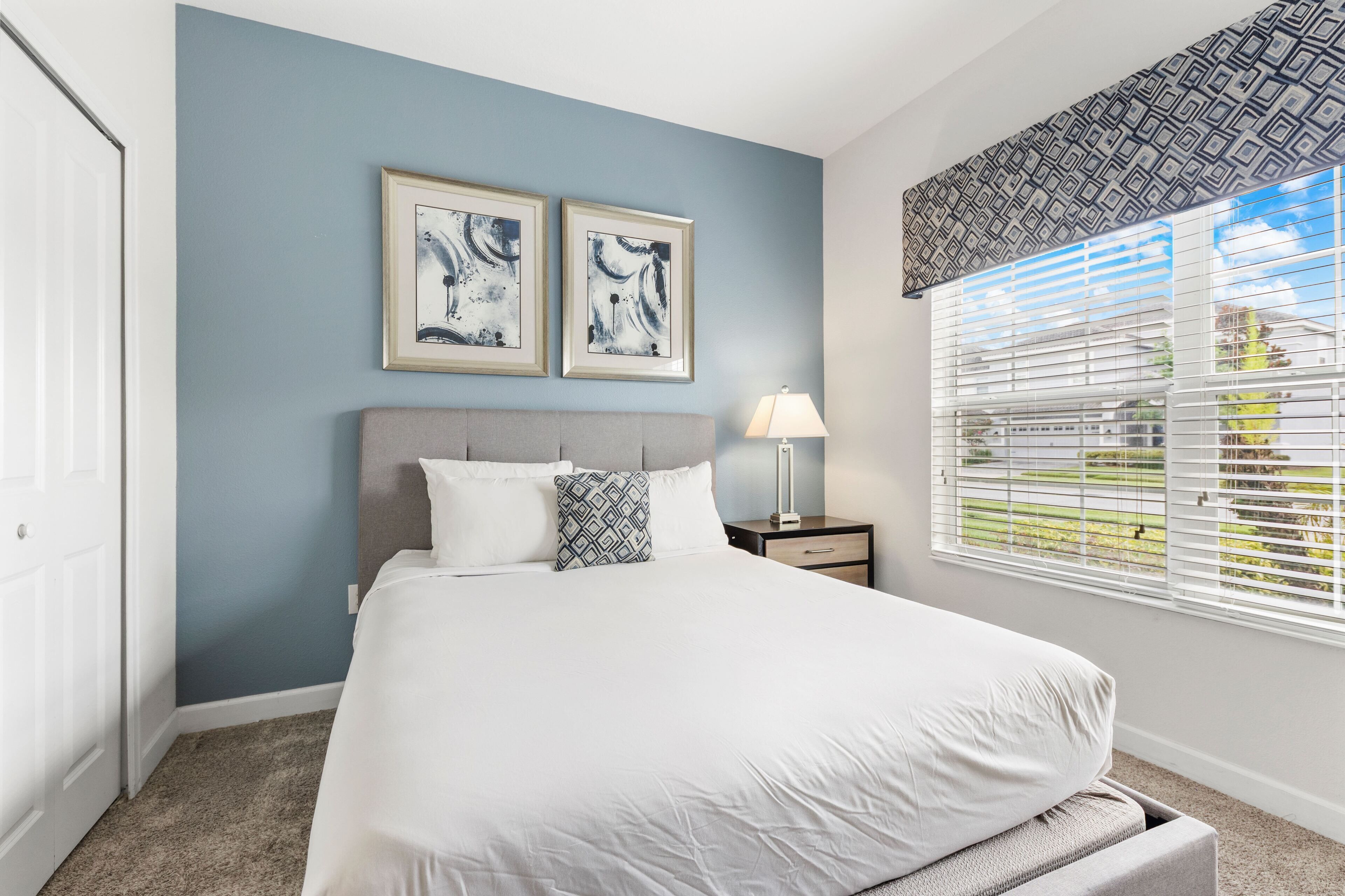 A bedroom with a bed, a nightstand, a lamp, and two framed abstract paintings on the wall.