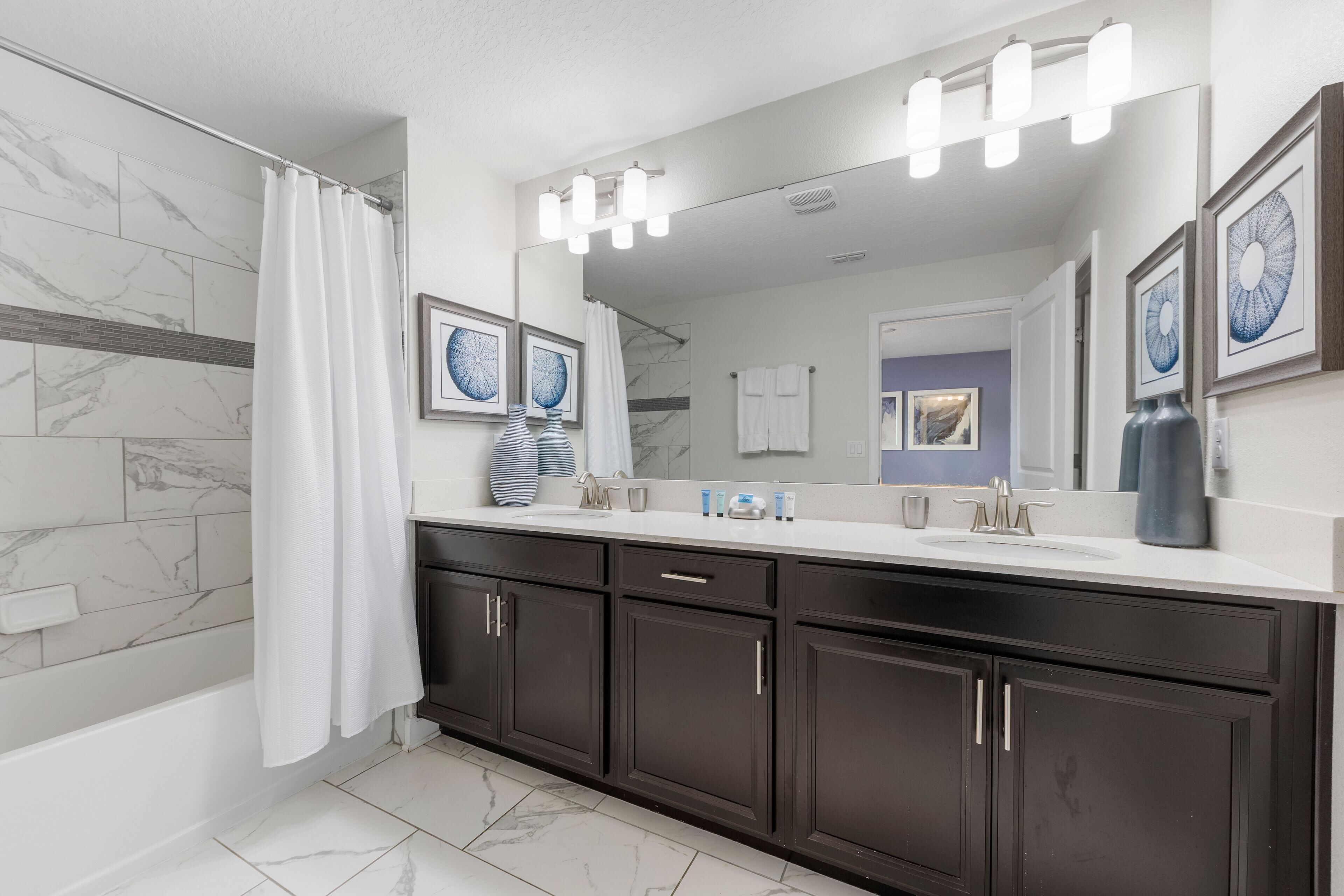 A modern bathroom with dark cabinets, a white sink, and a large mirror.