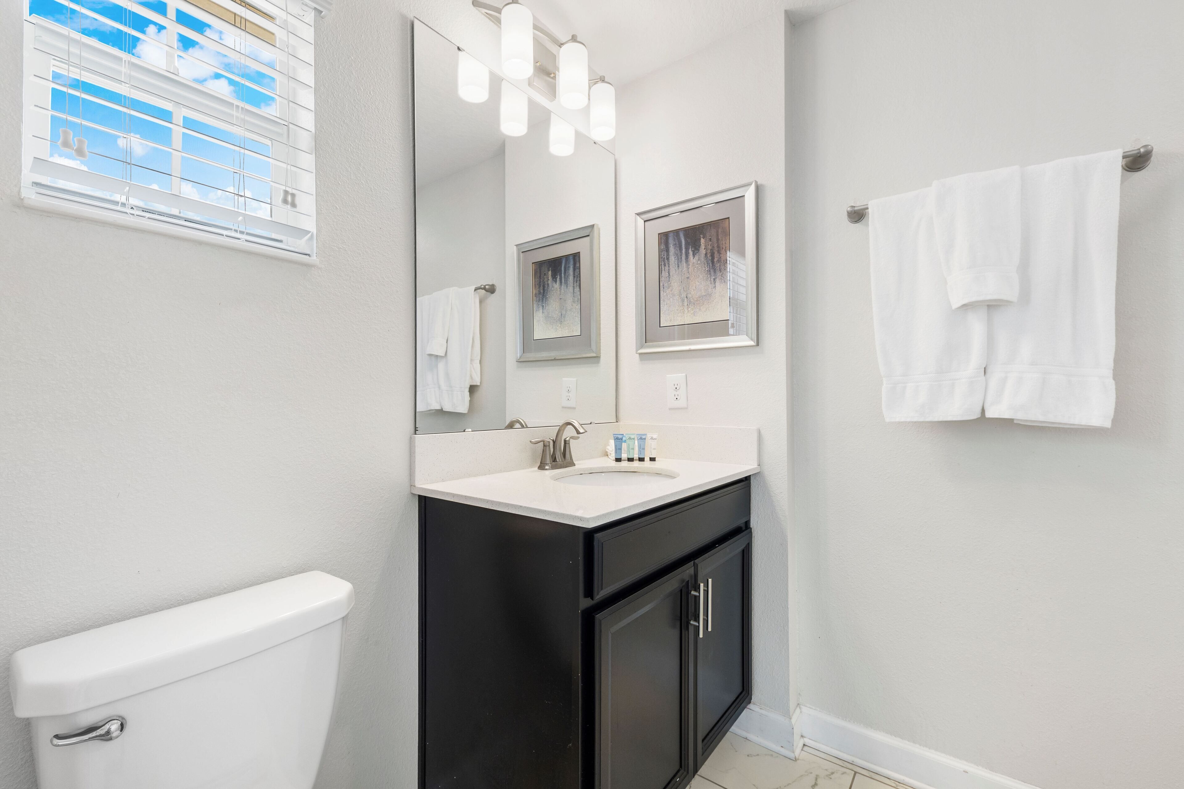 A bathroom with a white toilet, black cabinets, a white sink, and a mirror with framed artwork.