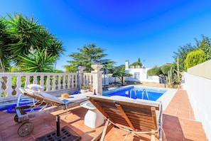 Un área junto a la piscina con sillones, una piscina pequeña y un pérgola con plantas.